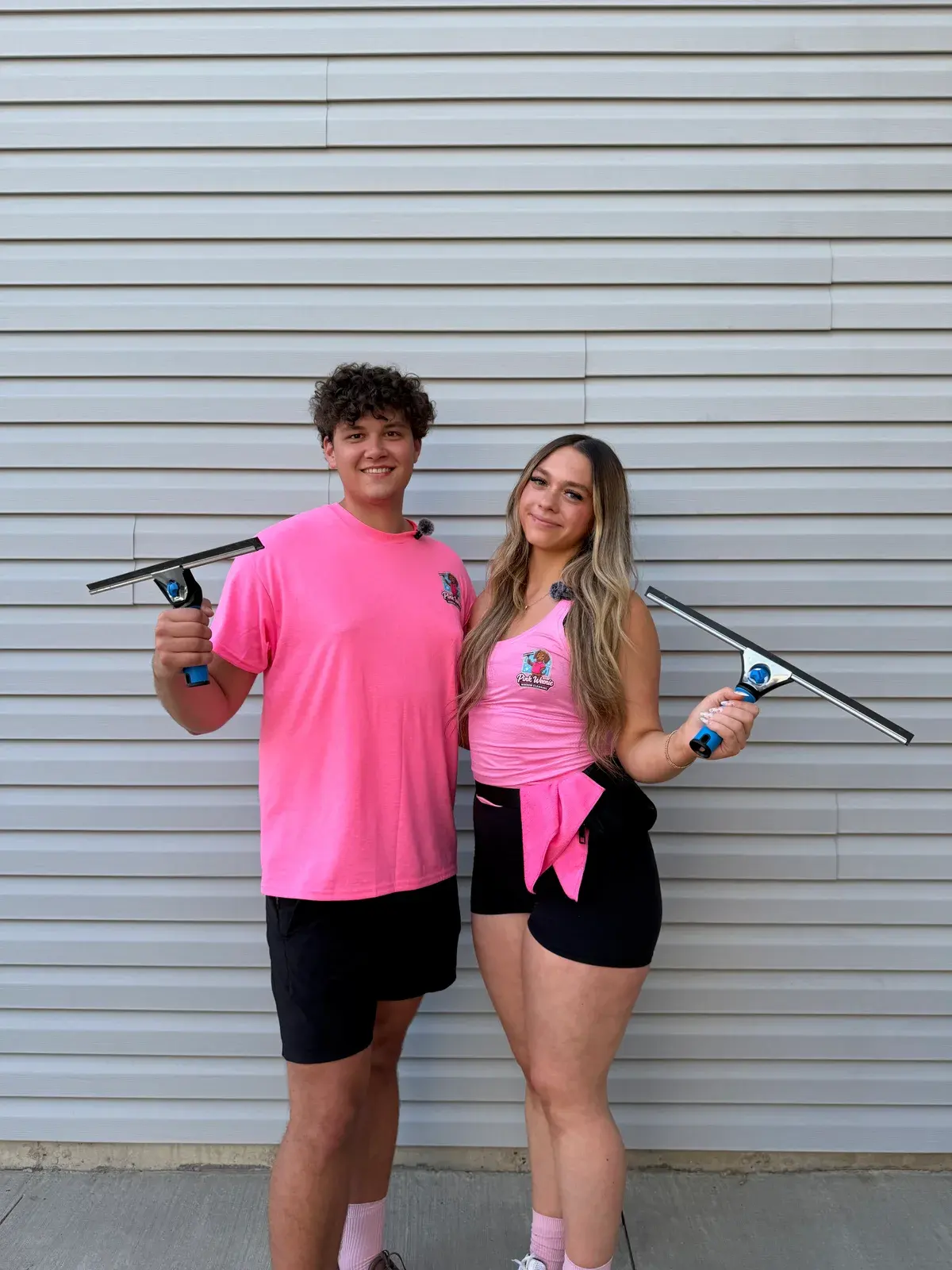 Vlad and Maya standing side by side in pink Pink Weenie Window Cleaning shirts, each holding a professional squeegee